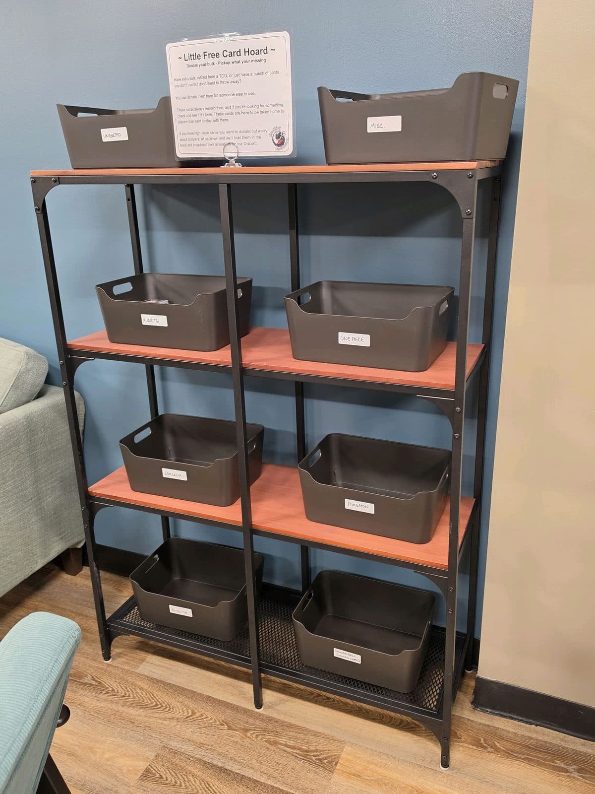 A shelving unit labelled Little Free Card Hoard, holding bins of donated cards sorted by game.