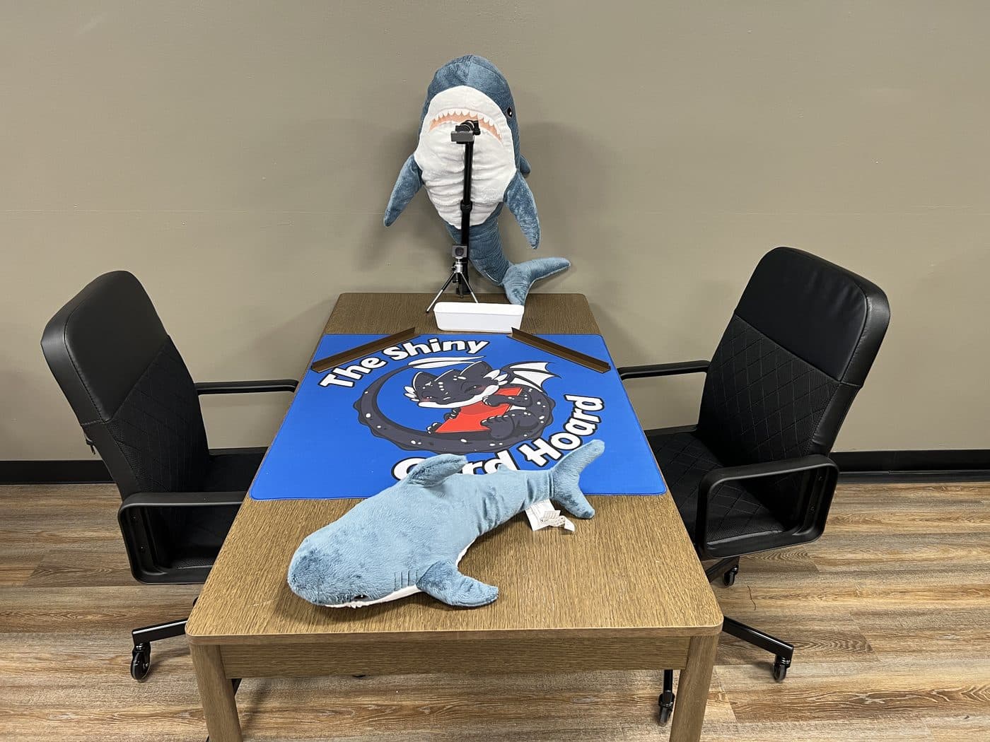 The top table, set with a Shiny Card Hoard playmat and two office chairs.